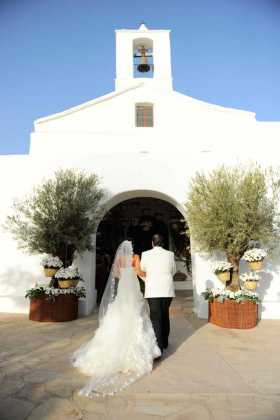 La novia con el padrino en la entrada decorada con cestos y flores.
