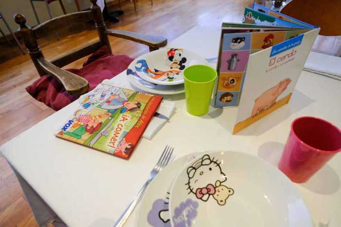 Restaurants Amics de la Infància, con vajilla infantil, cuentos y una trona dispuesta en la mesa